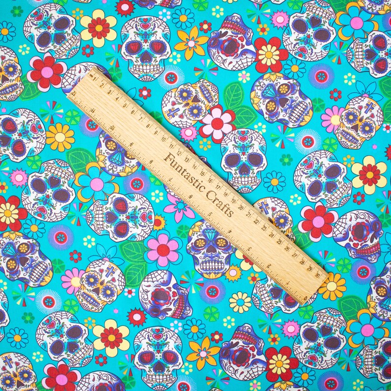 Op de afbeelding: Turquoise stof met een herhalend patroon van kleurrijke suiker schedels en bloemen. De stof is perfect voor knutselprojecten zoals kleding, accessoires en decoratie.