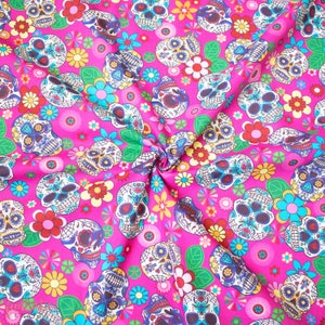 Op de afbeelding: Roze stof met een herhalend patroon van kleurrijke suiker schedels en bloemen. De schedels hebben ingewikkelde ontwerpen en zijn omringd door fel roze, gele en blauwe bloemen.
