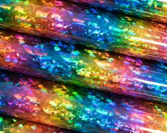 Op de afbeelding: Close-up van verschillende rollen iriserend, holografisch materiaal. Het materiaal reflecteert een spectrum aan kleuren, waaronder rood, oranje, geel, groen, blauw en paars. Het oppervlak heeft een getextureerd, gebroken uiterlijk, waardoor een glinsterend effect ontstaat.