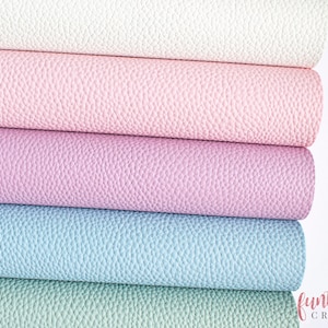 Puede incluir: Cuatro rollos de piel sintética en diferentes colores pastel: blanco, rosa, morado claro y azul claro. La piel tiene una superficie texturizada y granulada.
