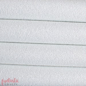Puede incluir: Primer plano de una tela de piel sintética blanca con una superficie texturizada y granulada. La tela está doblada en tres partes, mostrando la textura desde diferentes ángulos.