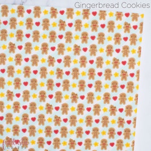 May include: A white fabric with a repeating pattern of gingerbread men, red hearts, and yellow stars. The background is a light blue color. The text "Gingerbread Cookies" is at the top of the image.