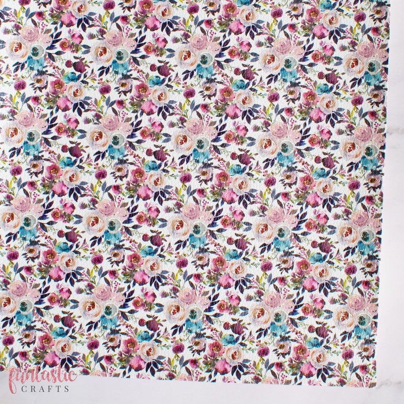 May include: White fabric with a repeating pattern of pink, blue, and purple watercolor flowers. The flowers are arranged in a random pattern and are surrounded by green leaves.