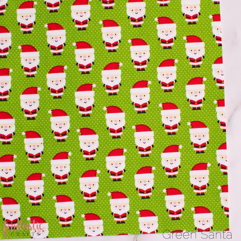 May include: Green fabric with a repeating pattern of white cartoon Santas wearing red hats. The fabric has a subtle white polka dot pattern.