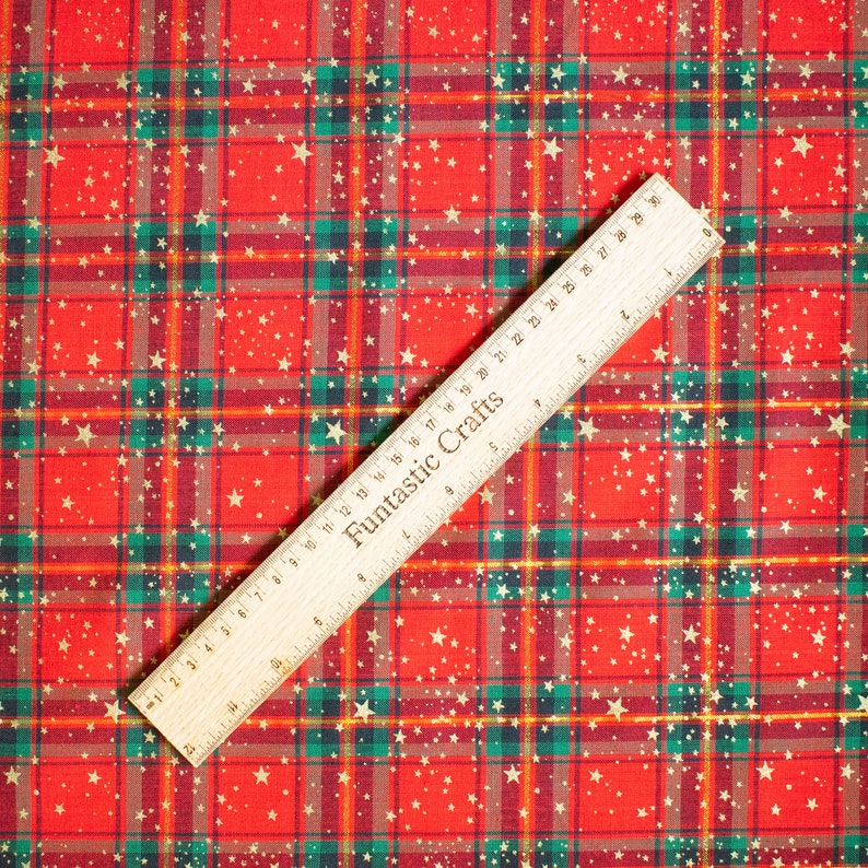 K&ouml;nnte beinhalten: Roter und gr&uuml;ner karierter Stoff mit goldenen Glitzersternen. Ein Holzlineal mit der Aufschrift "Funtastic Crafts" liegt auf dem Stoff.
