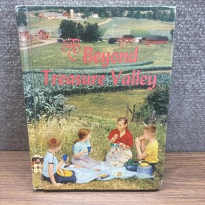 May include: A hardcover book titled The Beyond Treasure Valley featuring a cover illustration of three children having a picnic on a blue blanket in a grassy field with a rural farm landscape in the background, including red barns and green trees.