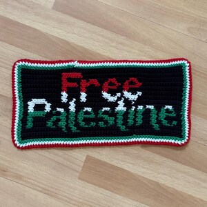 May include: Crocheted black rectangle with the words "Free Palestine" in red, white, and green. The border is red, white, and green. The item is handmade.