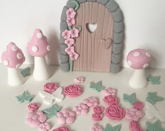 May include: A set of pink and white fondant fairy garden decorations, including a miniature door, mushrooms, flowers, and leaves.