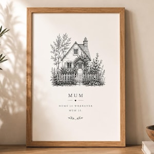 Puede incluir: Una lámina enmarcada con una ilustración en tinta negra y blanca de una casa de campo con valla de madera y árboles. El texto dice MUM, HOME IS WHEREVER MUM IS, con un pequeño corazón y detalles florales decorativos bajo la ilustración.