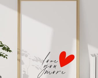 May include: A gold framed print with the text "love you more" in black script and a red heart in the center.
