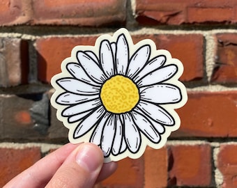 May include: A white daisy sticker with a yellow center. The daisy is drawn in a simple, cartoon style.
