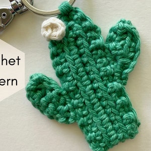 May include: A green crocheted cactus keychain with a white crocheted flower on top. The keychain has a silver metal clasp.