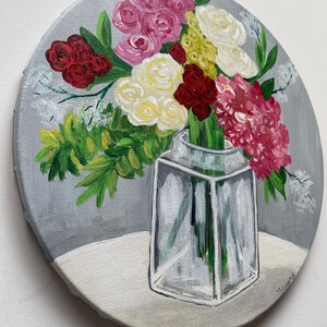 May include: A painting of a bouquet of flowers in a clear glass vase. The flowers are pink, white, red, and yellow. The vase is on a white surface. The background is gray.