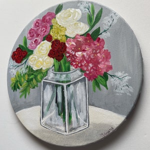 May include: A painting of a bouquet of flowers in a clear glass vase. The flowers are pink, white, red, and yellow. The vase is on a white surface with a gray background. The painting is signed "Y. Gawa" in the lower right corner.