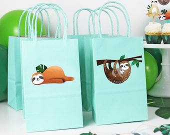 May include: Pale blue gift bags with twisted paper handles. Each bag features a sloth illustration. One shows a sloth resting, the other shows a sloth with a baby sloth hanging from a tree branch. Green balloons and decorations are in the background.
