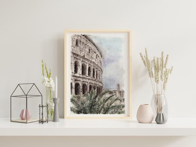 May include: Watercolor print of the Colosseum in Rome, Italy, framed in a light wood. The artwork depicts the ancient amphitheater with architectural details and a soft, muted color palette. The print is displayed on a white shelf with decorative items.