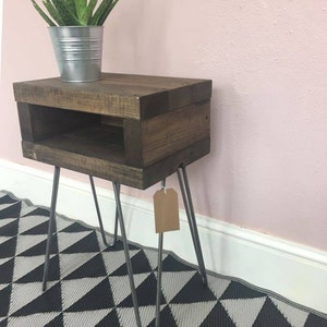 May include: A dark stained wooden side table with a lower shelf and metal hairpin legs. A small potted plant in a silver metal container sits on top. The table is on a black and white geometric patterned rug.