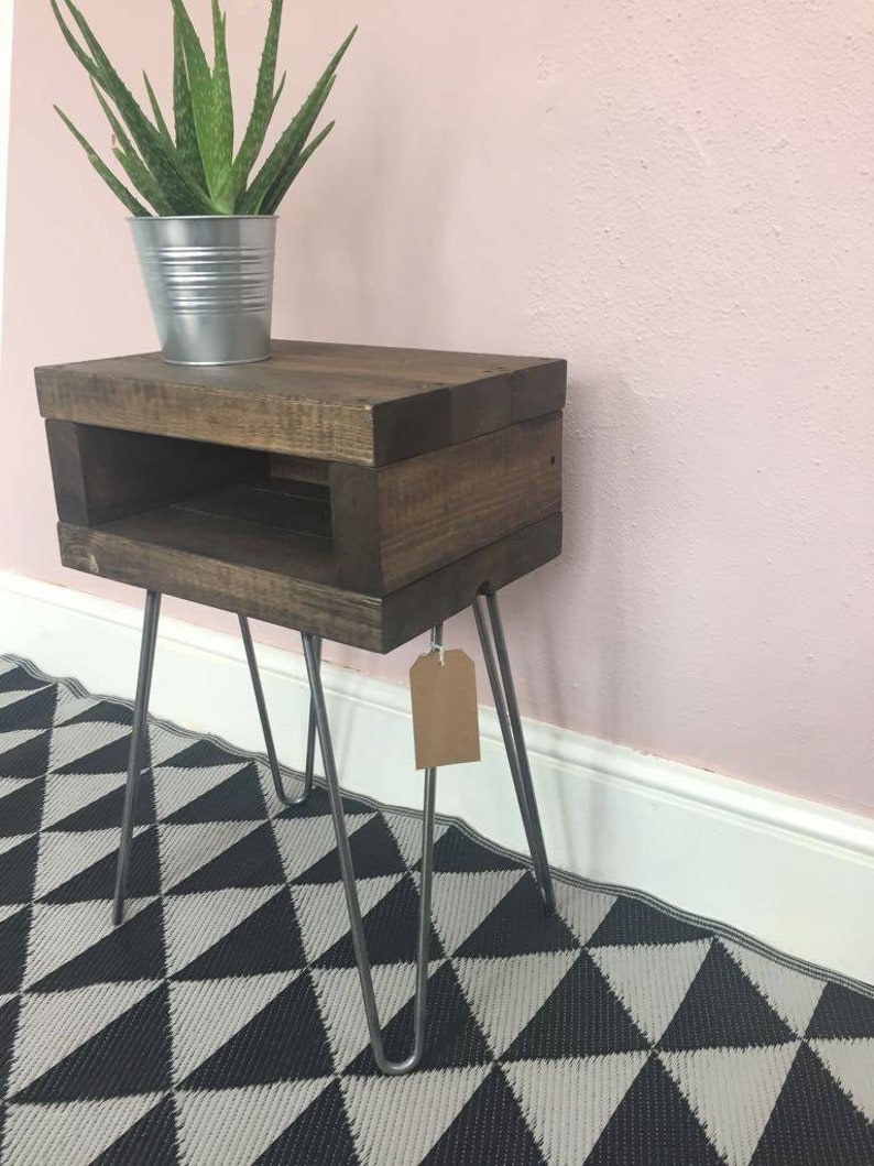 May include: A dark stained wooden side table with a lower shelf and metal hairpin legs. A small potted plant in a silver metal container sits on top. The table is on a black and white geometric patterned rug.