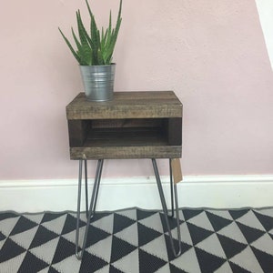 May include: A rustic, wooden side table with a dark stain, featuring a lower shelf and hairpin legs. A metal pot with a green plant sits on top. The table is approximately 24 inches tall.
