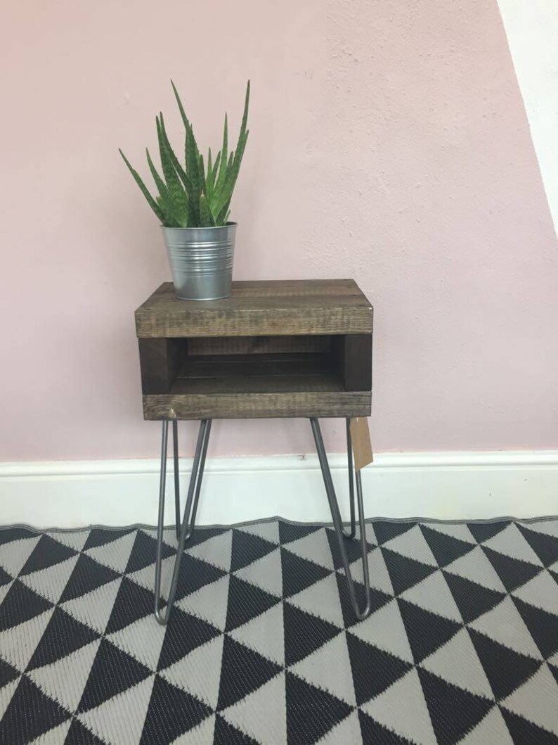 May include: A rustic, wooden side table with a dark stain, featuring a lower shelf and hairpin legs. A metal pot with a green plant sits on top. The table is approximately 24 inches tall.