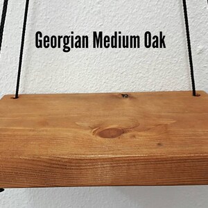May include: A rectangular wooden shelf with a medium oak finish, suspended by black ropes. The shelf has rounded edges and visible wood grain. The text "Georgian Medium Oak" is displayed above the shelf.