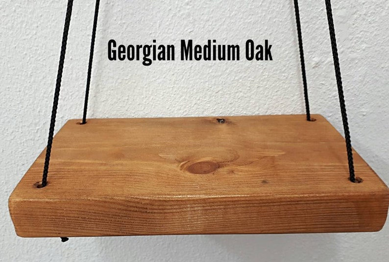 May include: A rectangular wooden shelf with a medium oak finish, suspended by black ropes. The shelf has rounded edges and visible wood grain. The text "Georgian Medium Oak" is displayed above the shelf.