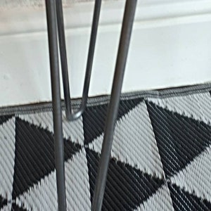 May include: Close-up of a wooden table with metal hairpin legs. The tabletop is a dark brown color, and the legs are silver. The table is set on a black and white geometric patterned rug.