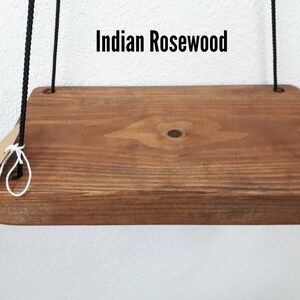 May include: A rectangular wooden shelf made of Indian Rosewood, suspended by black rope. The shelf has a natural wood grain finish and a small tag is attached to the rope. The text "Indian Rosewood" is displayed above the shelf.