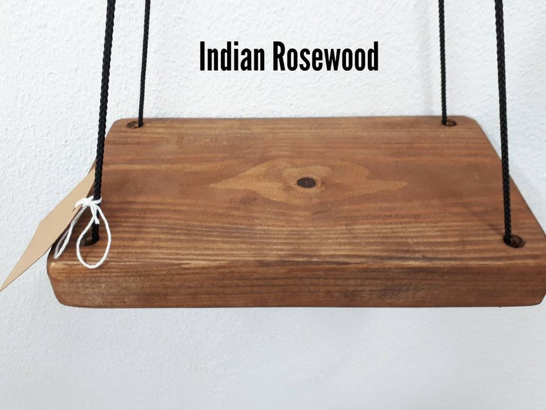 May include: A rectangular wooden shelf made of Indian Rosewood, suspended by black rope. The shelf has a natural wood grain finish and a small tag is attached to the rope. The text "Indian Rosewood" is displayed above the shelf.
