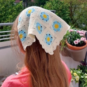 Könnte beinhalten: Ein weißes Häkelbandana mit blauen und gelben Blumen. Das Bandana ist um den Kopf einer Person gebunden.