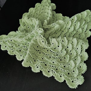 May include: A light green crocheted baby blanket with a scalloped edge.