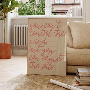 May include: A beige framed print with the text "you can't control the wind, but you can adjust the sails" written in pink cursive.