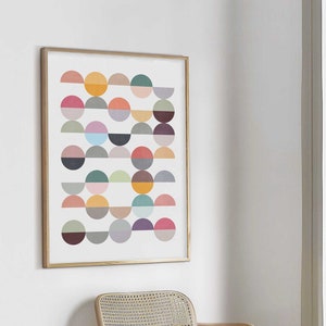 May include: A framed abstract print with a geometric pattern of colorful semi-circles in various shades of red, orange, yellow, green, blue, purple, and gray. The print is hanging on a white wall next to a light wood chair with a woven cane seat.