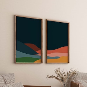 May include: Two framed abstract landscape prints with a dark blue background and colorful layers of green, yellow, orange, pink, and red. The prints are hung on a white wall.