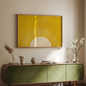 Könnte beinhalten: Ein grünes Mid-Century-Modern-Schrank mit drei Türen steht auf einem Holzboden. Ein gelber und weißer abstrakter Sonnenabdruck hängt an der Wand über dem Schrank. Ein kleiner grüner Hocker steht im Vordergrund.