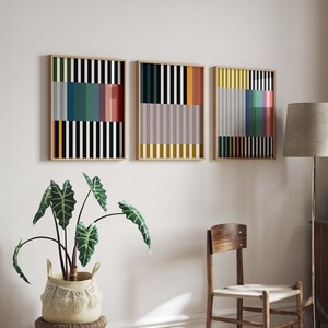 Pode incluir: Tr&ecirc;s impress&otilde;es geom&eacute;tricas abstratas com listras verticais em v&aacute;rias cores, incluindo preto, branco, vermelho, amarelo, azul e verde. As impress&otilde;es s&atilde;o emolduradas em madeira natural e penduradas em uma parede branca.