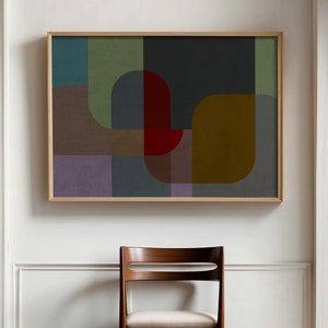 May include: Abstract geometric art print in a wooden frame with muted colors of green, blue, red, brown, and purple. The print is hanging on a white wall above a wooden chair.