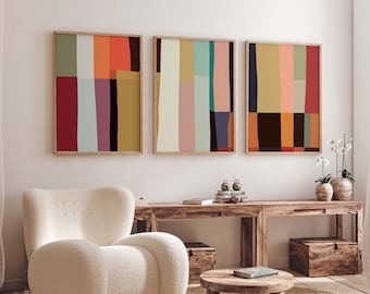 Op de afbeelding: Drie abstracte kunstprints met geometrische vormen in verschillende kleuren, waaronder rood, oranje, geel, groen, blauw en bruin. De prints zijn ingelijst in natuurlijk hout en hangen aan een witte muur boven een houten consoletafel.