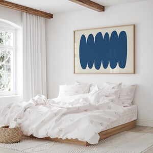 May include: A white bed with a pink duvet cover and white pillows. The duvet cover has a subtle star pattern. A framed print with a blue abstract design hangs on the wall above the bed.