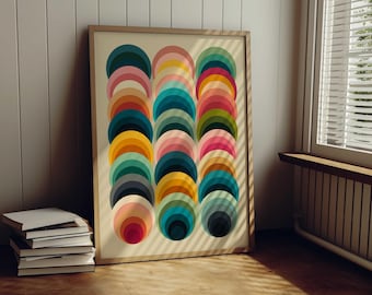 Puede incluir: Una lámina de arte enmarcada que presenta tres columnas verticales de semicírculos superpuestos en una vibrante paleta de azul verdoso, rosa, amarillo, naranja, verde y azul oscuro. La obra se exhibe en un marco de madera clara con diseño geométrico.