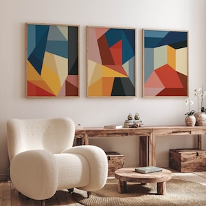 以下が含まれることがあります： 赤、黄、青、緑、茶色の色が混ざった、抽象的な幾何学模様の芸術作品が3点。作品は木製の額縁に収められ、白い壁に掛けられています。壁の下には、木製のテーブルと白いアームチェアがあります。