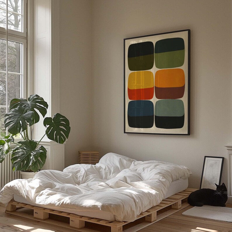 May include: A bedroom scene featuring a bed made of wooden pallets, covered with white bedding. A framed abstract art piece with colorful geometric shapes hangs on the wall. A large potted plant and a black cat complete the cozy interior.
