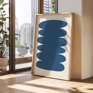 May include: A framed abstract print with a stack of blue oval shapes on a cream background.