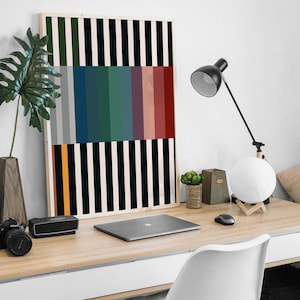 Pode incluir: Uma impress&atilde;o de arte abstrata emoldurada com listras verticais pretas e brancas e uma fileira de listras coloridas no meio. A impress&atilde;o est&aacute; pendurada em uma parede branca acima de uma mesa com um laptop, uma l&acirc;mpada e uma planta em vaso.