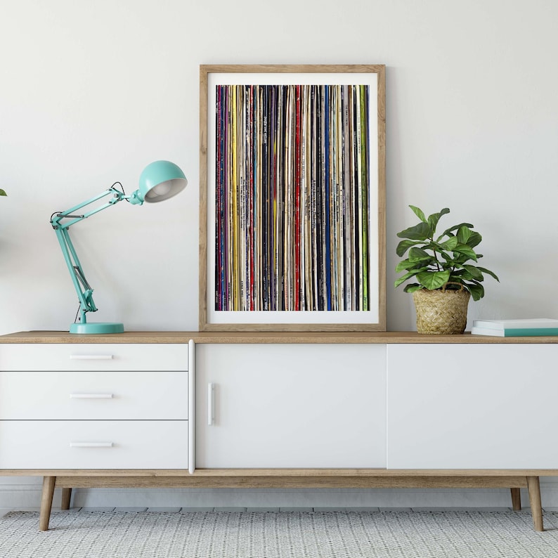 Pu&ograve; includere: Una cassettiera bianca con tre cassetti e una porta scorrevole. Una stampa incorniciata di una disposizione verticale colorata di dischi in vinile &egrave; appesa sopra la cassettiera. Una piccola pianta in vaso e una lampada da scrivania blu sono sulla cassettiera.