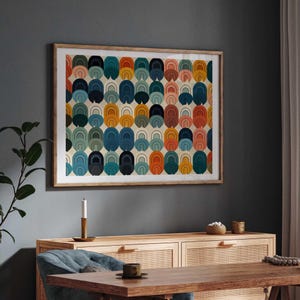 May include: A rectangular wall art print in a light wood frame featuring a repeating pattern of stacked arch shapes in shades of orange, teal, navy blue, and soft pink against a cream background, displayed in a horizontal orientation.