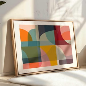 Puede incluir: Impresión de arte geométrico abstracto con un diseño colorido que presenta tonos de naranja, amarillo, verde, azul, rojo y rosa. La impresión está enmarcada en un marco de madera claro.