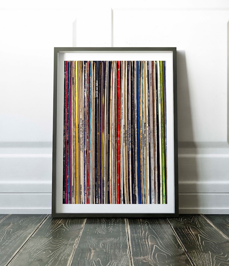 Pu&ograve; includere: Una stampa incorniciata di un muro di dischi in vinile colorati. I dischi sono disposti verticalmente in una griglia. La cornice &egrave; nera e lo sfondo &egrave; bianco.