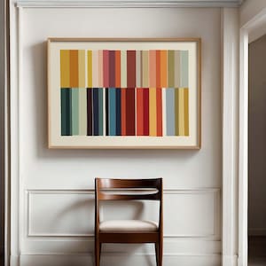 Puede incluir: Una impresi&oacute;n art&iacute;stica abstracta enmarcada con rayas verticales en varios colores, incluyendo naranja, amarillo, rojo y azul, cuelga sobre una silla de madera con asiento blanco. La obra de arte est&aacute; en un marco de madera clara, y la silla tiene un acabado de madera oscura.