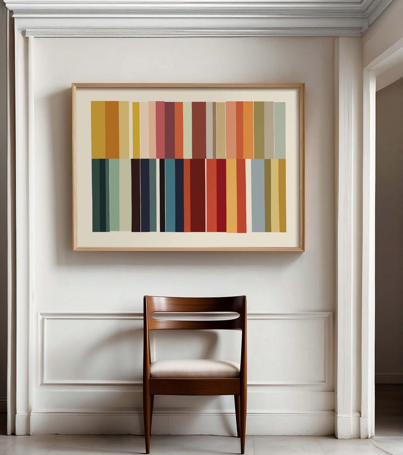 Puede incluir: Una impresi&oacute;n art&iacute;stica abstracta enmarcada con rayas verticales en varios colores, incluyendo naranja, amarillo, rojo y azul, cuelga sobre una silla de madera con asiento blanco. La obra de arte est&aacute; en un marco de madera clara, y la silla tiene un acabado de madera oscura.